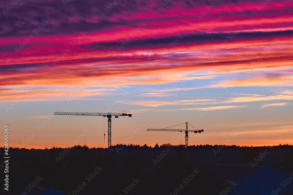 The tower cranes on the beautiful sunset sky background. 