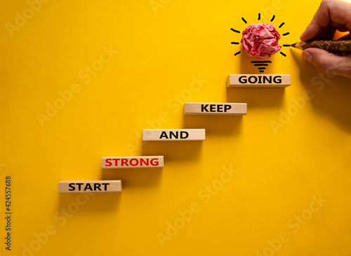 Start strong and keep going symbol. Concept words 'Start strong and keep going' on wooden blocks on a beautiful yellow background. Businessman hand. Business, motivational and start strong concept.