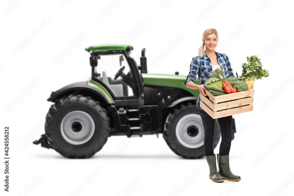 Fototapeta premium Female farmer with a crate full of organic vegetables standing in front of a tractor