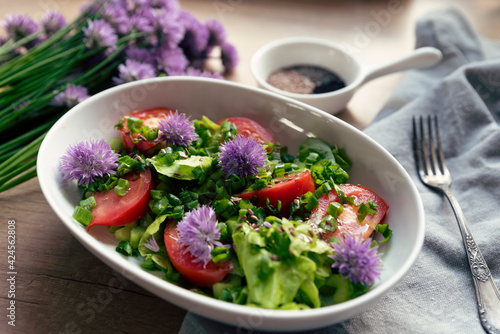 Fototapeta Naklejka Na Ścianę i Meble -  Salad for breakfast. Vegetarian meal with vegetables, lettuce, tomatoes and flowers of chives, Sping in a kitchen, on a table and bowl. Close up.