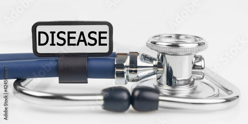 On the white surface lies a stethoscope with a plate with the inscription - DISEASE