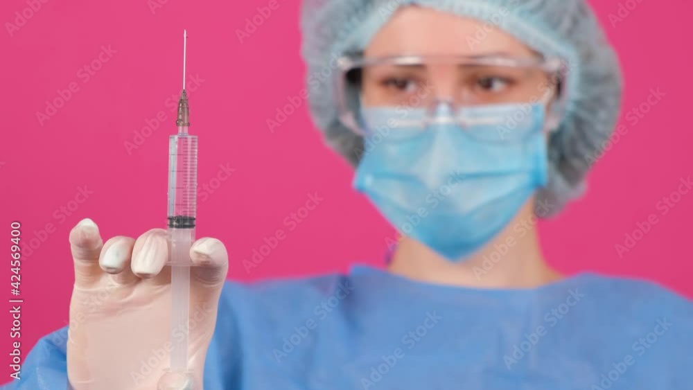 Professional female doctor holds a syringe with a vaccine on a pink background. Professional female doctor holds a syringe with a vaccine on a pink background.