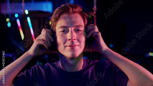 A cute young gamer guy puts a headset on his head in the computer room and smiles