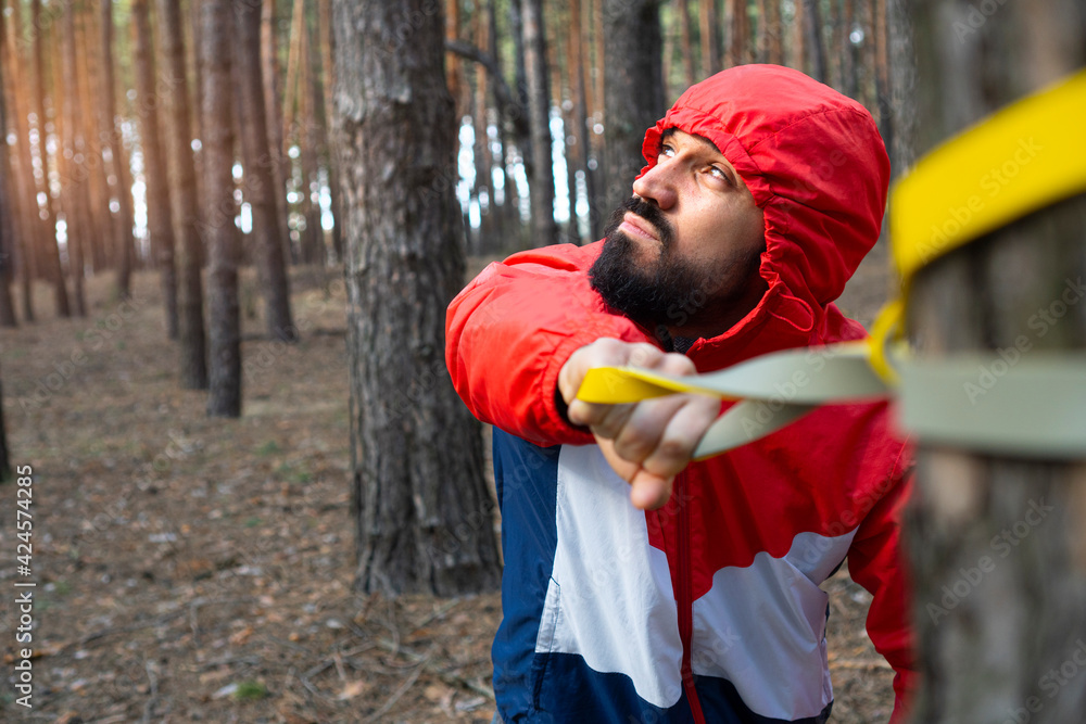 Bearded man workout with the resistance band in a morning forest. Exercises on a fresh air during quarantine. Exercise equipment for outdoor fitness. Bearded man workout with the resistance band in a morning forest. Exercises on a fresh air during quarantine. Exercise equipment for outdoor fitness.
