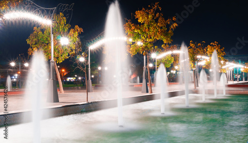 autumn city park at night, fountains, trees with yellow leaves and street lights