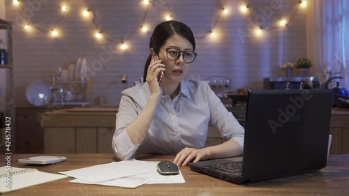 business overwork people deadline and technology concept. angry asian korean businesswoman with laptop calling on smartphone at night home kitchen and screaming. hard working lady employee arguing photo