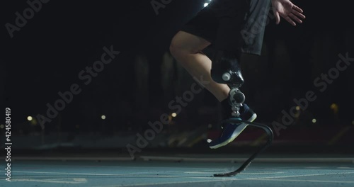 Cinematic close up shot of disable man with legs prosthesis is warming up before run with dedication on car track at night. Concept of handicapped people active lifestyle, determination, motivation. photo