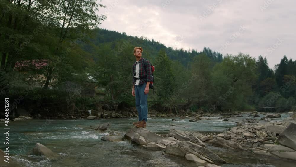Tourist standing on rocky shore of river. Joyful man looking green landscape Tourist standing on rocky shore of river. Joyful man looking green landscape