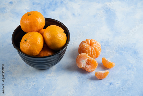 Close up photo of Clementine mandarins whole or peeled in black bowl