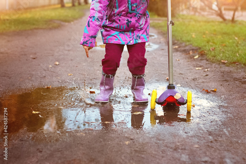 children's feet of girl in puddle in rubber purple boots next to scooter