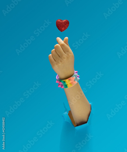 K pop concept. A girl hand with rainbow pyramid studded bracelet showing fingers heart gesture. Red glittery heart above. Optimistic blue in background.