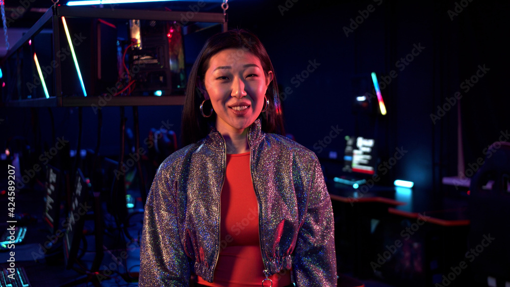 A smiling chinese woman in a short jacket with sequins poses for the camera in a computer club