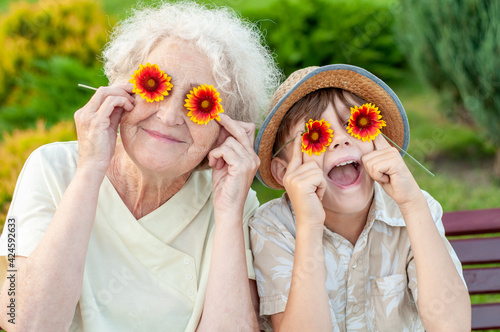 Boy and grandmother puts on the eyes of chamomile. Family holiday.Laughing grandson with his beloved grandmother spend leisure time outdoors. An elderly woman and a grandchild. Summer spring time