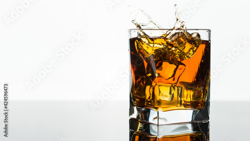 Glass of Whiskey or Brandy. Splash in a Glass on white background. Alcohol Drink. Clear ice in cube shape. Frozen water. Ice maker. Fake or Artificial acrylic or plastic ice cubes.