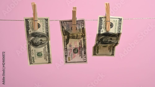 paper american dollars hang on a clothesline, attached with a wooden clothespin. Pink background, money laundering concept