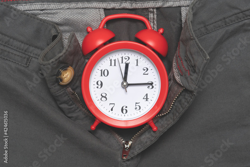 Red alarm clock is on open zipper of grey pants. Close up. Gender, sexual menstrual concept.
