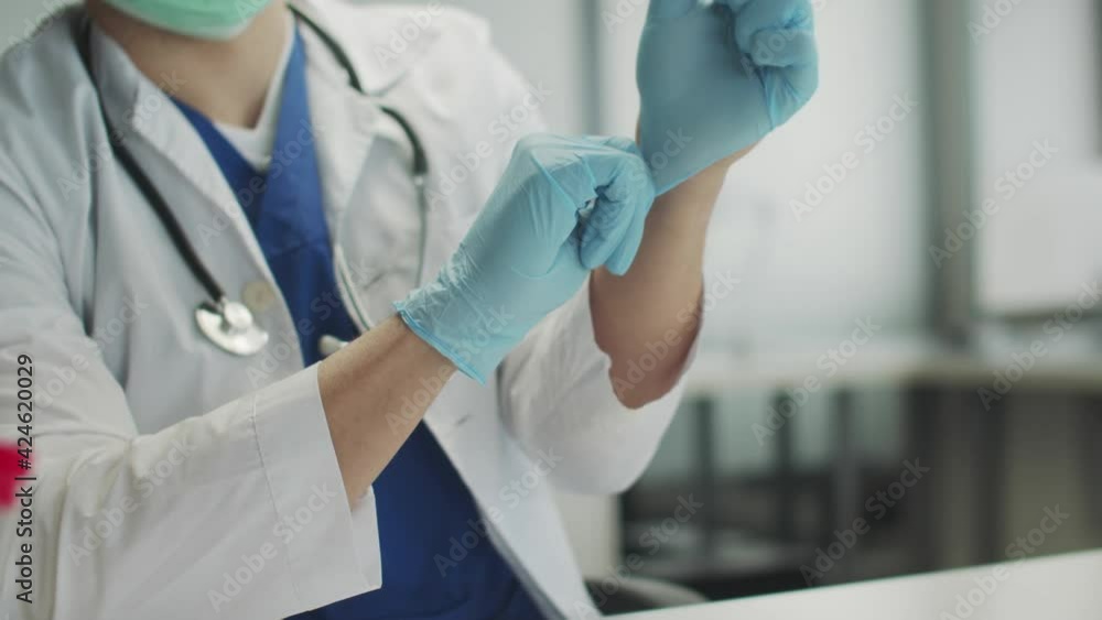 The doctor in the medical office is preparing to receive patients and carry out vaccination against covid-19. He puts on blue rubber protective gloves. The doctor in the medical office is preparing to receive patients and carry out vaccination against covid-19. He puts on blue rubber protective gloves.