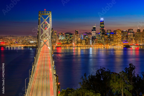 Bay Bridge with light trails and downtown San Francisco viewed from Treasure Island at sunset and reflections on the water in the Bay, long exposure