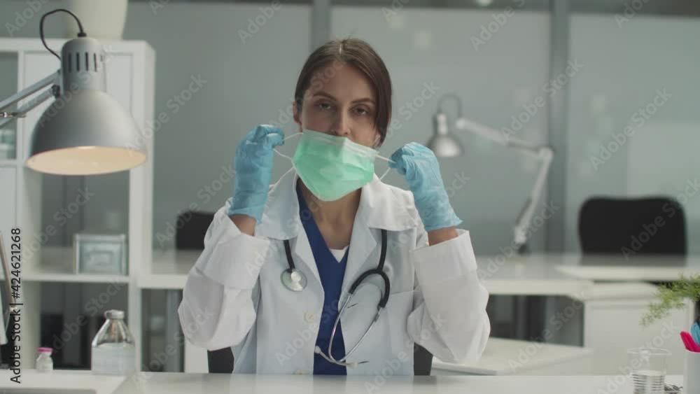 After a working shift at the clinic, the doctor removes the medical mask from her face and smiles pleasantly After a working shift at the clinic, the doctor removes the medical mask from her face and smiles pleasantly