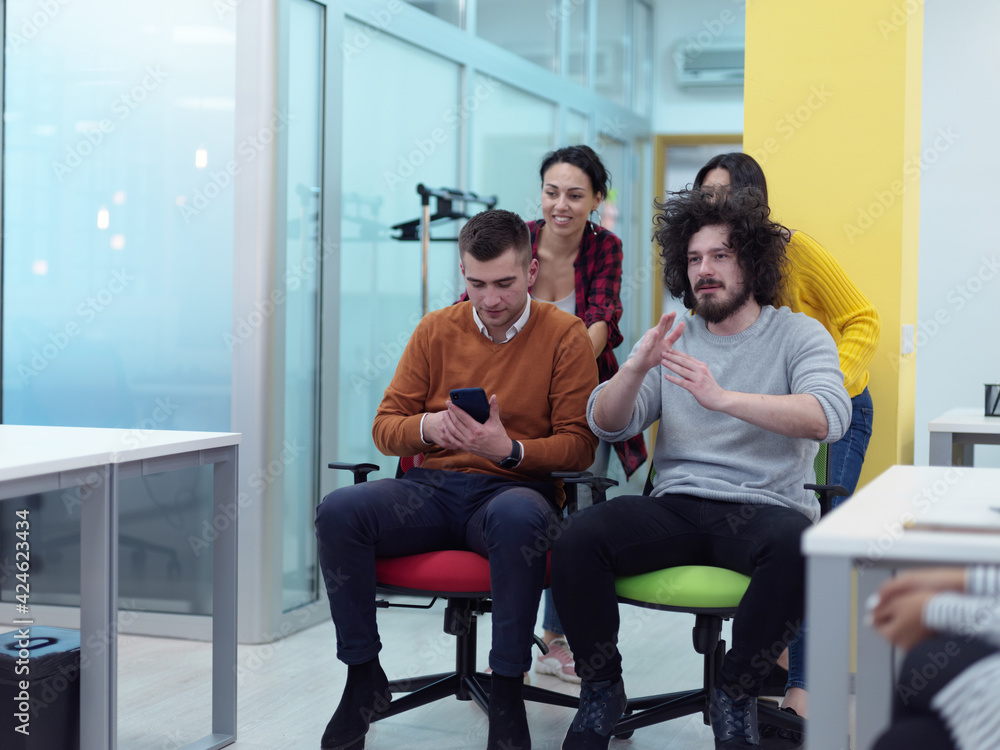 Multiethnic startup group at office chair race Multiethnic startup group at office chair race