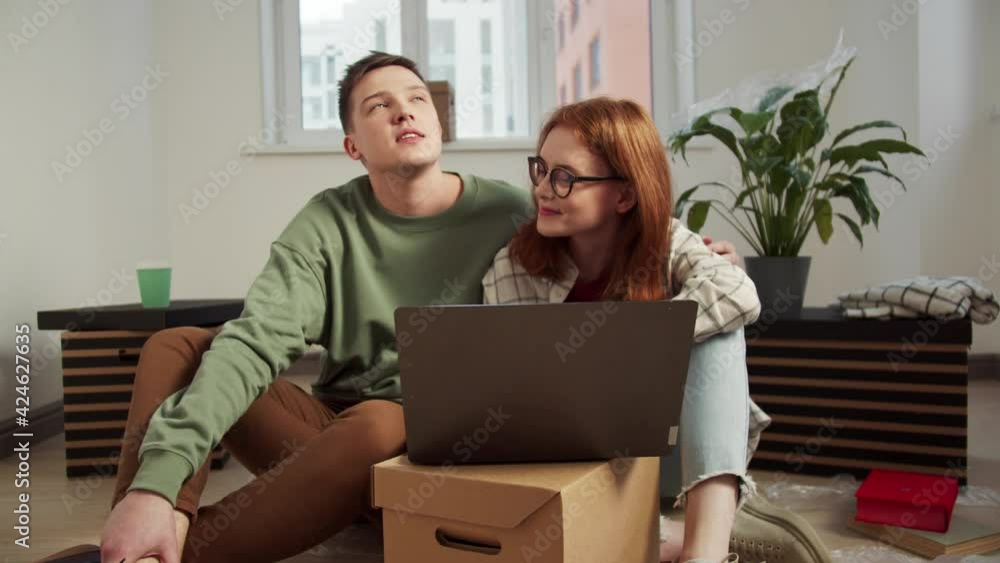 A couple is sitting near a computer on the floor, smiling and looking around A couple is sitting near a computer on the floor, smiling and looking around