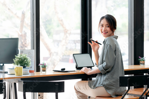 Young beautiful asian woman smiling, loooking at camera and waving while sitting at counter table in cafe.