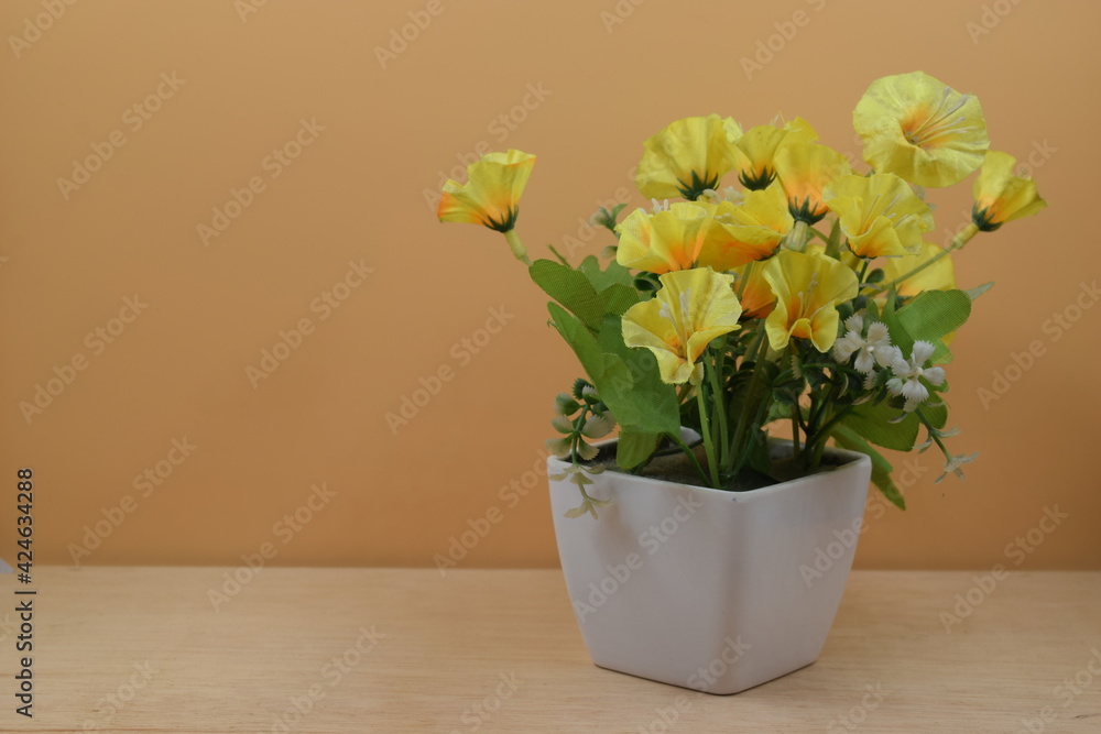 flor amarilla en florero blanco, sobre superficie de madera y fondo naranja. en posición horizontal y alineada a la izquierda
