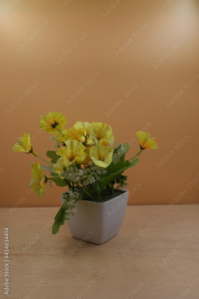 flor amarilla en florero blanco, en posición vertical, alineada a la izquierda. sobre superficie de madera y fondo naranja 
