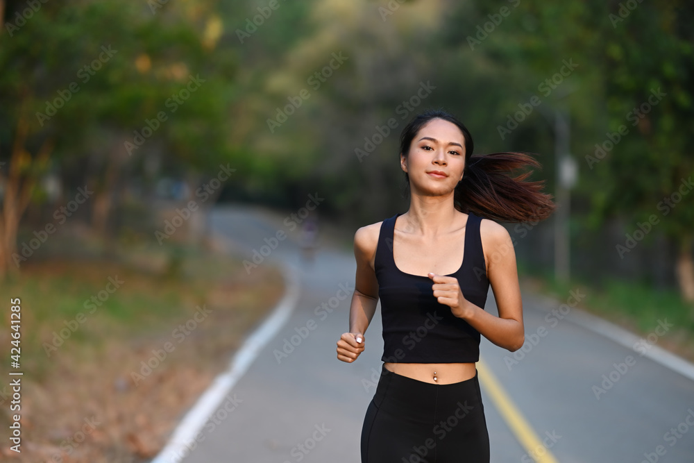 Athletic woman running in city park at the evening.
