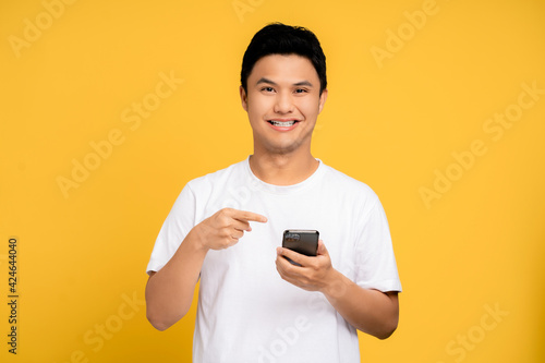 Young Asian man wearing a white T-shirt is using a smartphone. He was smiling and very happy. Isolated background. © PBXStudio