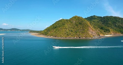 Aerial View sideways motorboat tropical. Aerial view: fast moving speed boat wake on clear blue sea water, turquoise building, ship shore, waves, green forest