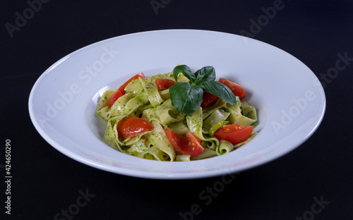 Spaghetti pasta with herbs and tomatoes. In a white plate on a black background
