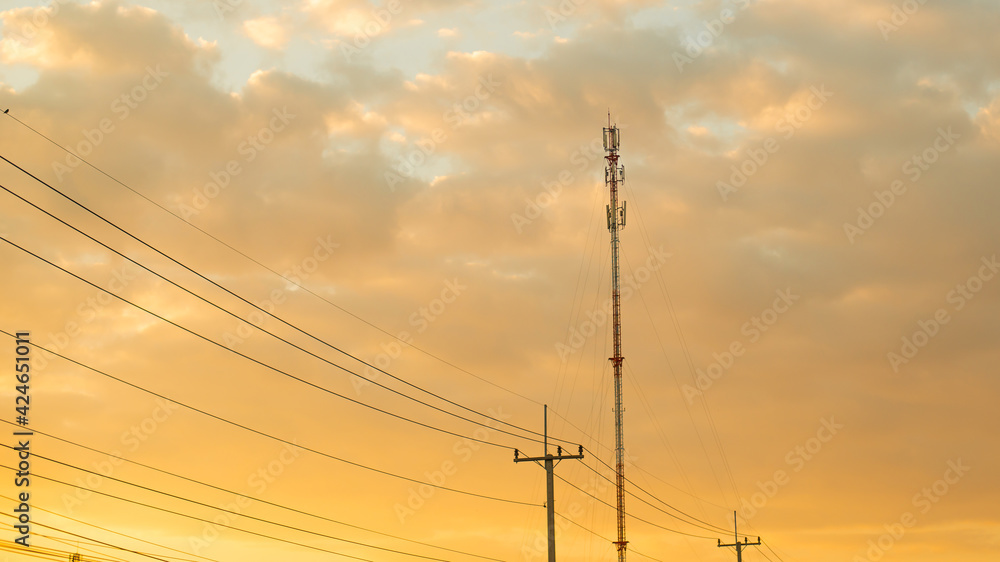 The golden sky in the evening has wires and telephone poles.
