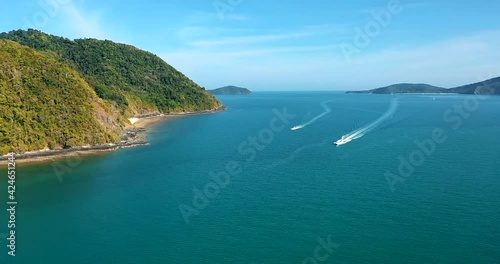 Aerial View sideways motorboat tropical. Aerial view: fast moving speed boat wake on clear blue sea water, turquoise building, ship shore, waves, green forest