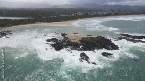 Rocky Headland With Foamy Breaking Waves Overlooking Township Of Sawtell Beach In North Coast Of New South Wales, Australia. - Aerial Pullback Shot photo