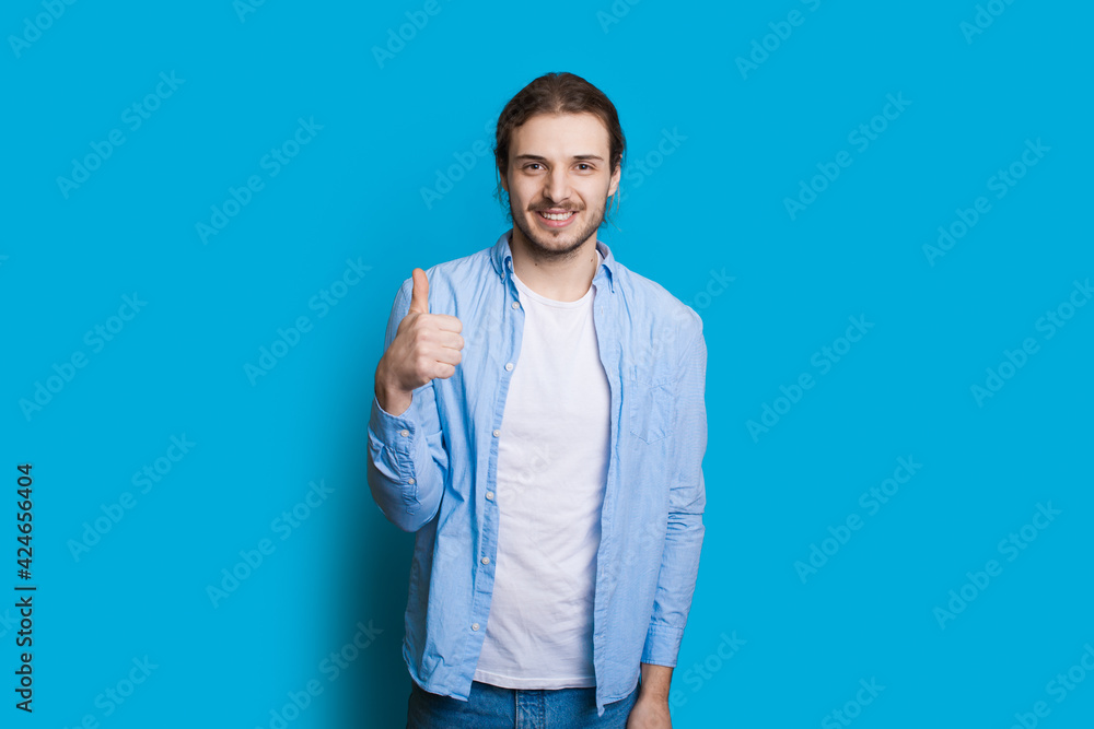 Caucasian man with beard and long hair is gesturing the like sign on a blue studio wall Caucasian man with beard and long hair is gesturing the like sign on a blue studio wall