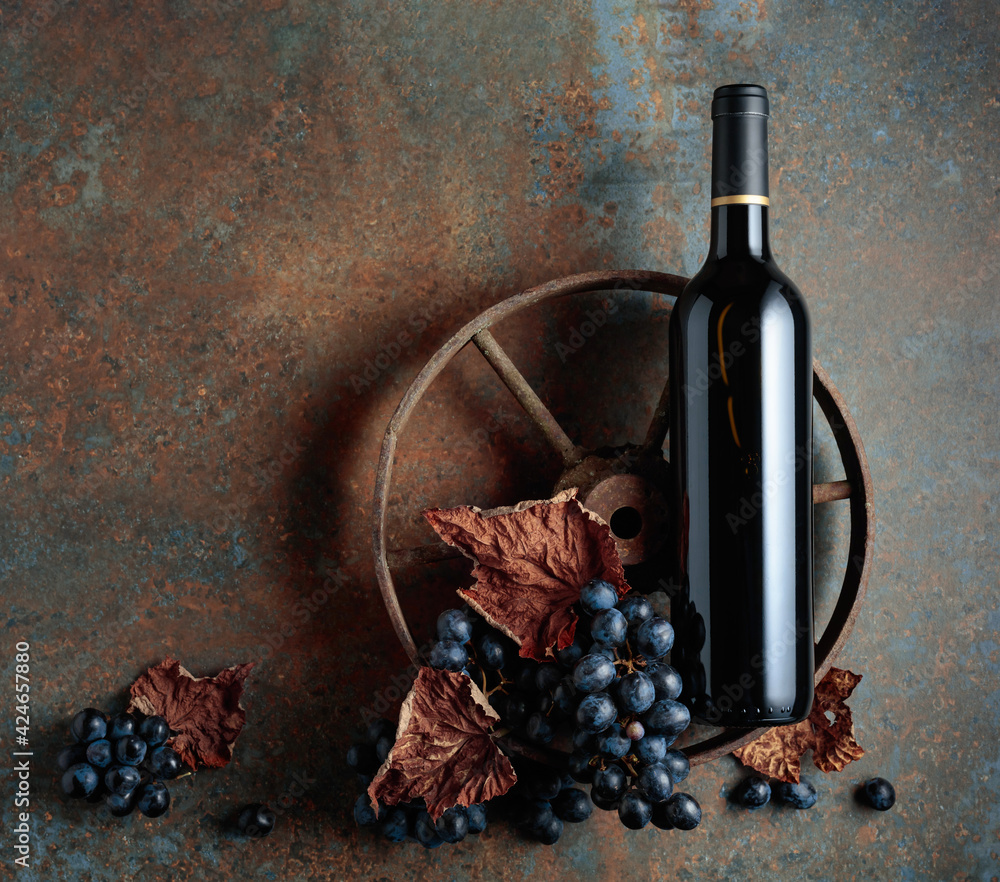 Bottle of red wine with an old rusty wheel. - obrazy, fototapety, plakaty 