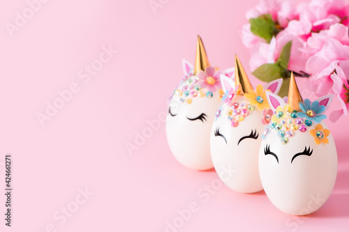 Unicorn eggs. Three Easter eggs in the form of a unicorn and a branch of a blossoming apple tree on a pink background with copy space. 