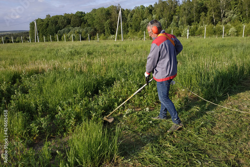 Man mows the grass with a trimmer, tall grass in a meadow, handmade in the garden.