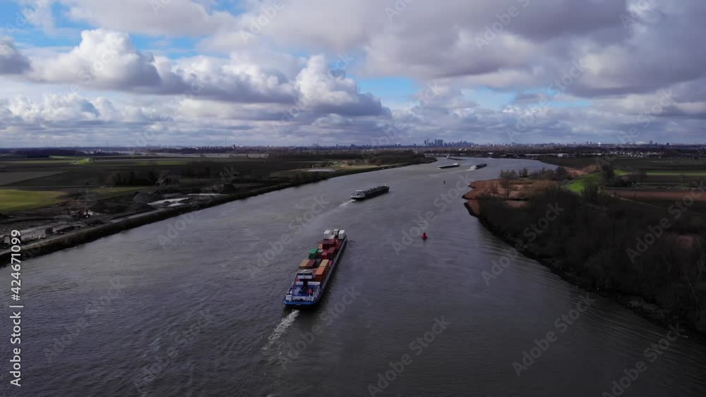 Ship Carrying Containers Sailing In Tranquil River Canal Of Oude Maas Near Shore Of Puttershoek, Netherlands. - Wide Shot Ship Carrying Containers Sailing In Tranquil River Canal Of Oude Maas Near Shore Of Puttershoek, Netherlands. - Wide Shot