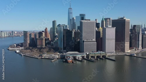 An aerial view of New York Harbor on a sunny day with blue skies. The drone camera facing lower Manhattan truck left and pan right over the waters with a Staten Island Ferry in the terminal.