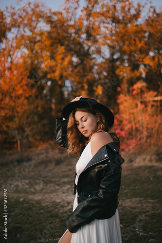 Beautiful young bride wearing stylish wedding dress with black hat and jacket in autumn forest.