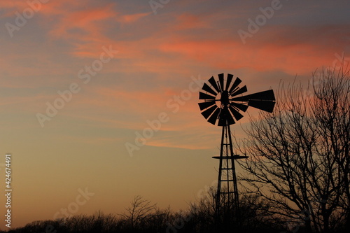 Kansas colorful Sunset with tree silhouette's farm Windmill, and a colorful sky with clouds out in the country north of Hutchinson Kansas USA.