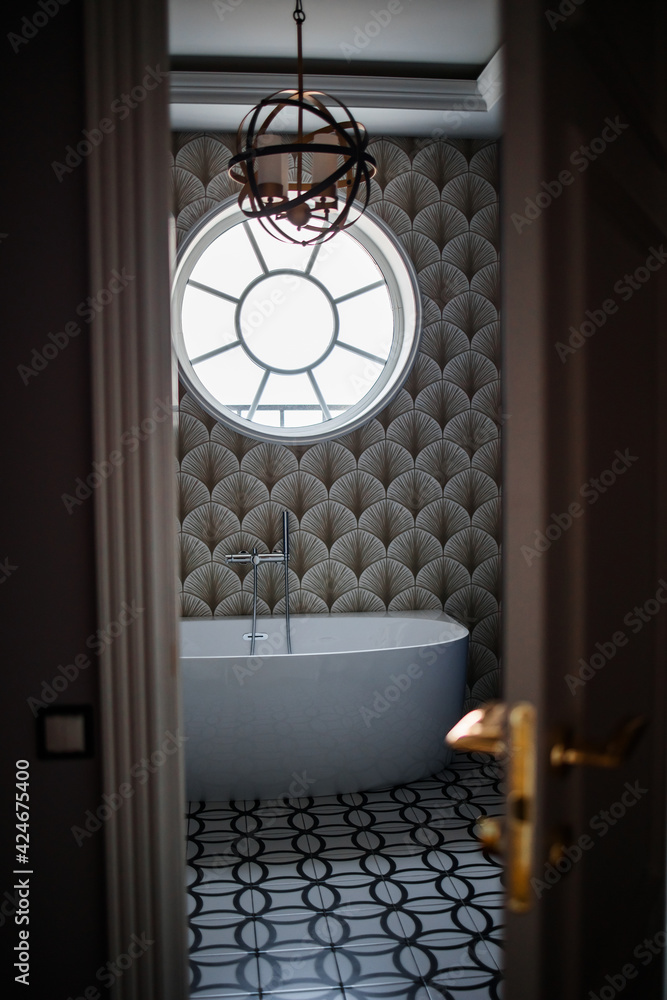 free-standing bath on the background of a round window with a round chandelier