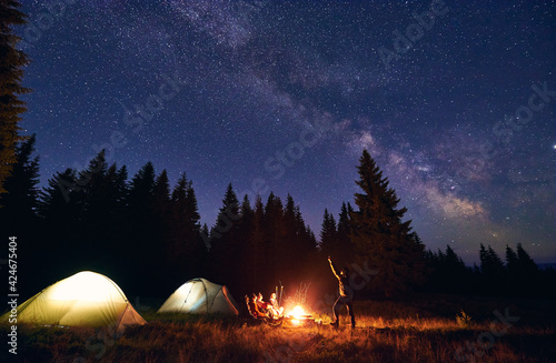 Man is showing his friends Milky Way over tent city. Outdoor recreation
