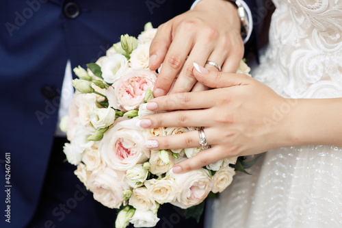 The bride and groom in wedding suits are holding together a wedding bouquet of white and lilac roses. Men's blue classic suit for men and girls white dress. Newlyweds without faces