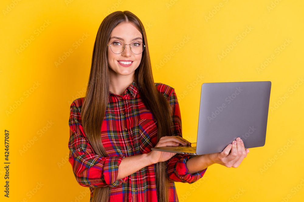 Portrait of nice optimistic brunette long hairdo lady hold laptop wear spectacles red shirt isolated on vivid yellow color background Portrait of nice optimistic brunette long hairdo lady hold laptop wear spectacles red shirt isolated on vivid yellow color background