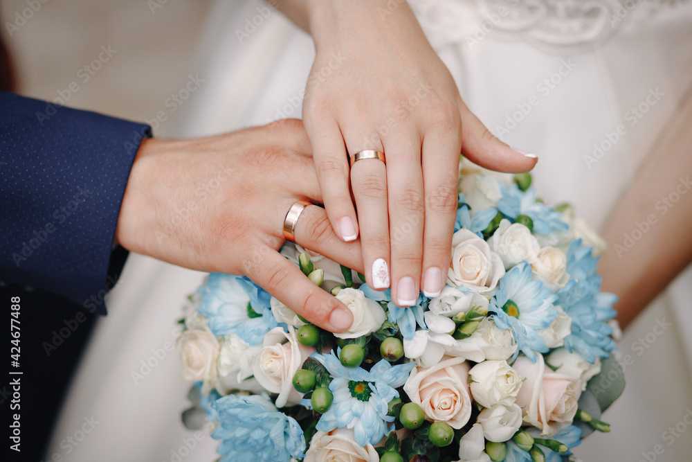 The bride and groom in wedding suits are holding together a wedding bouquet of white and blue roses. Men's blue classic suit for men and girls white dress. Newlyweds without faces The bride and groom in wedding suits are holding together a wedding bouquet of white and blue roses. Men's blue classic suit for men and girls white dress. Newlyweds without faces
