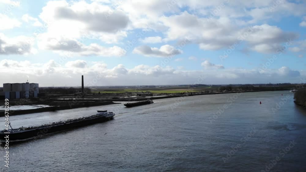 Industrial Barges Sailing At Oude Maas River Under Bright Sky With Fluffy White Clouds In Puttershoek, Netherlands. - aerial Industrial Barges Sailing At Oude Maas River Under Bright Sky With Fluffy White Clouds In Puttershoek, Netherlands. - aerial