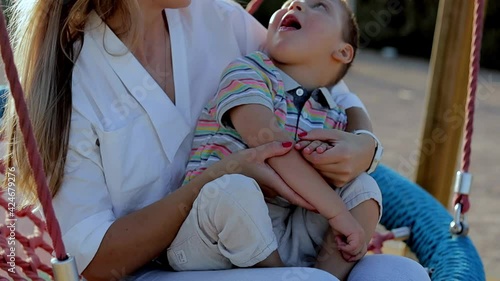 Happy mom proud of her son can walking outdoors. Kid with physical diability. Video of enjoy happy love family outdoors. Lovely mom ride on swing for person with diability with her son. Happy moments